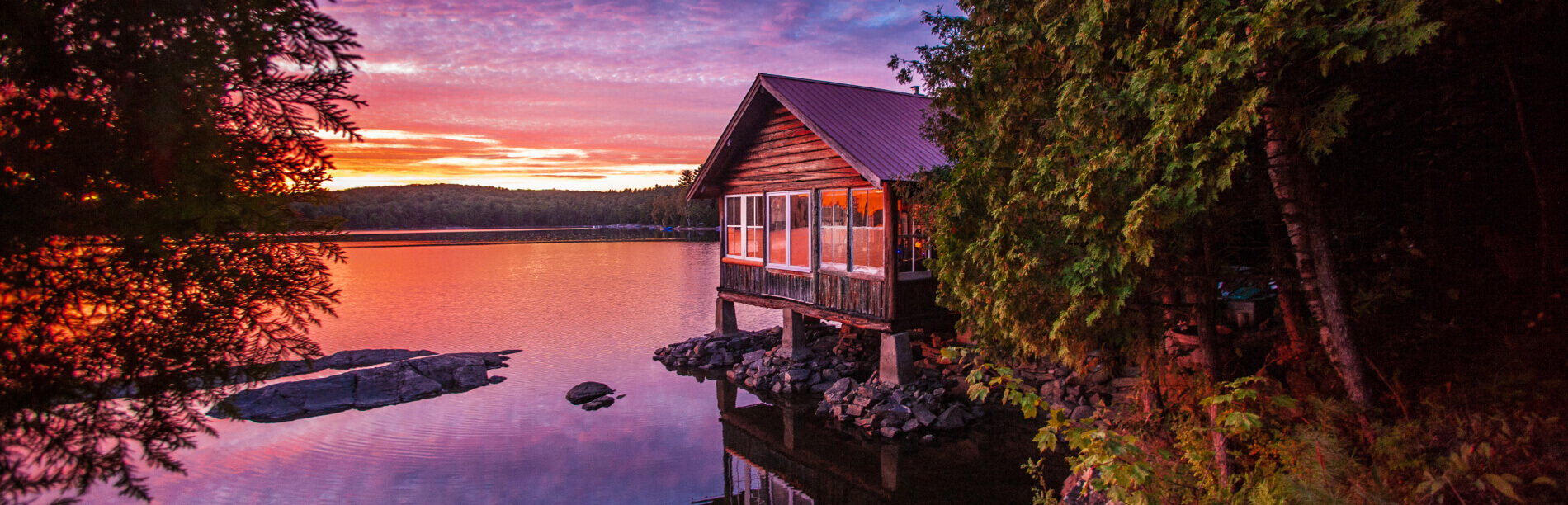 A sunset on a lake with a cottage.