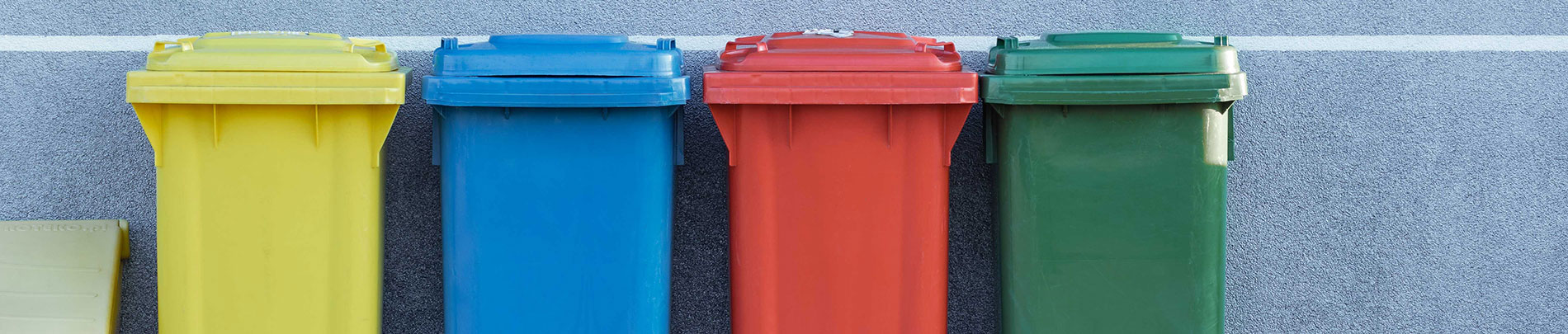 A series of colourful garbage and recycling bins lined up against a wall.